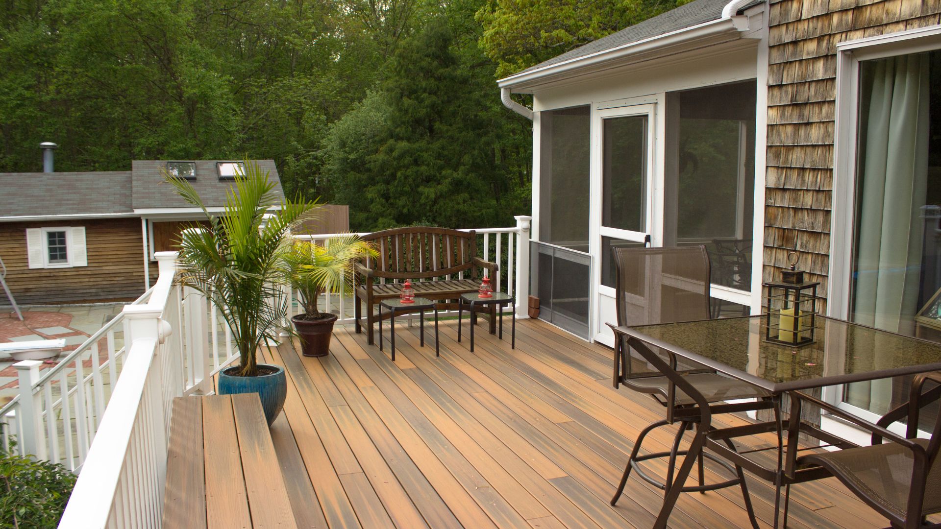 Wooden deck with patio furniture and palm plants near wooded backyard