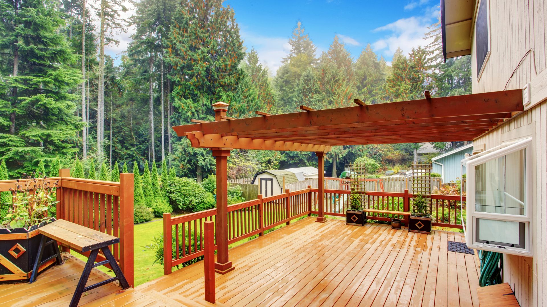 Wooden deck with pergola overlooking lush green forest and backyard