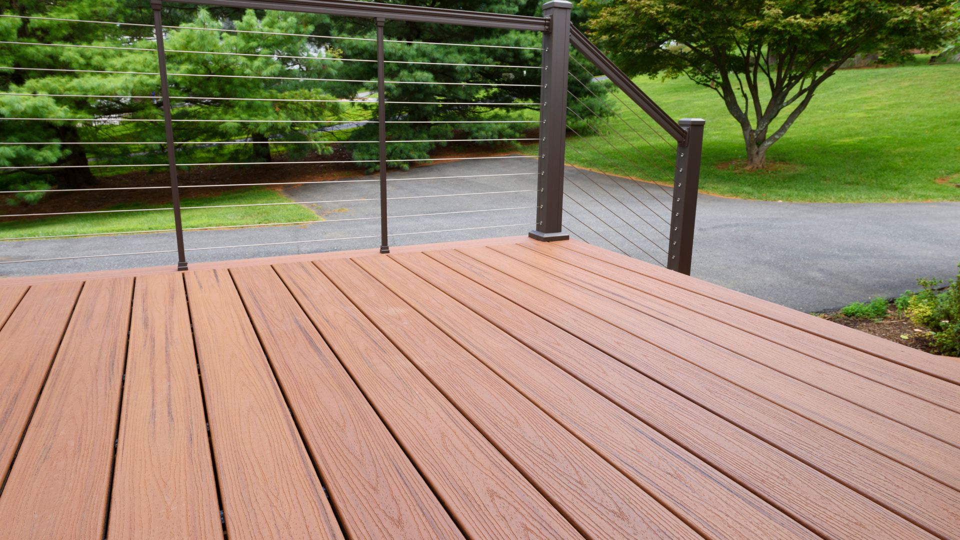 Modern wooden deck with metal cable railing overlooking green lawn