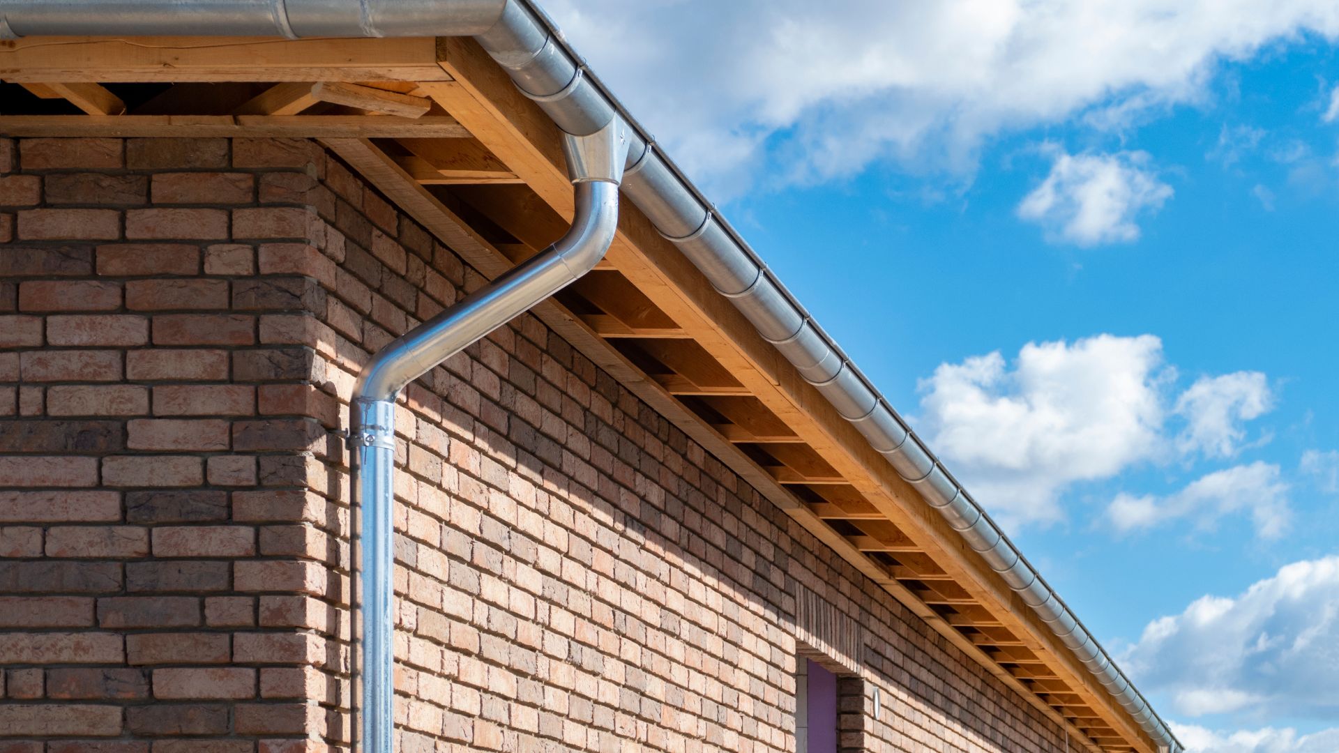 Brick building with metal gutters and wooden roof detail against blue sky