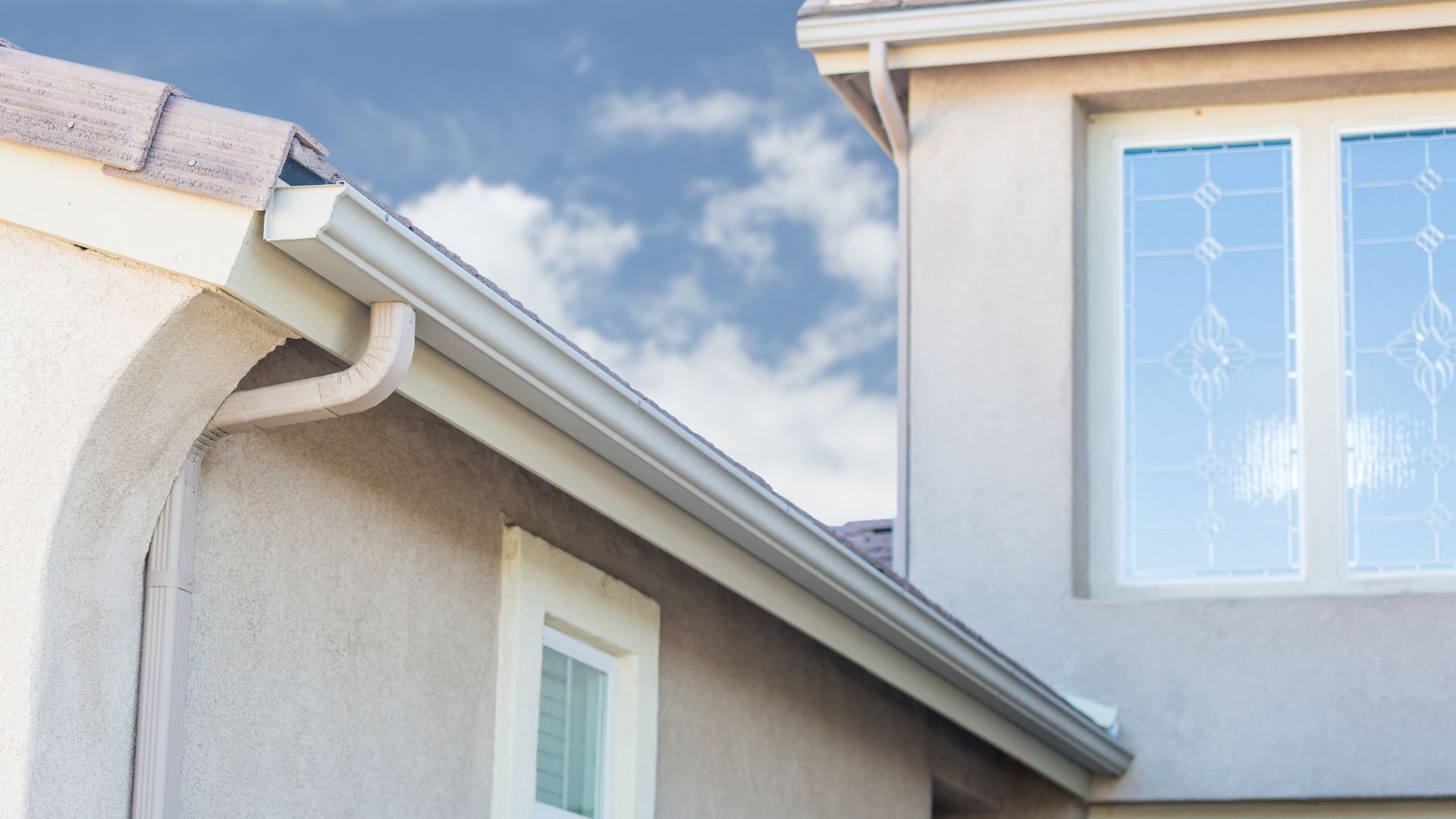White gutters on stucco house exterior with blue sky and windows