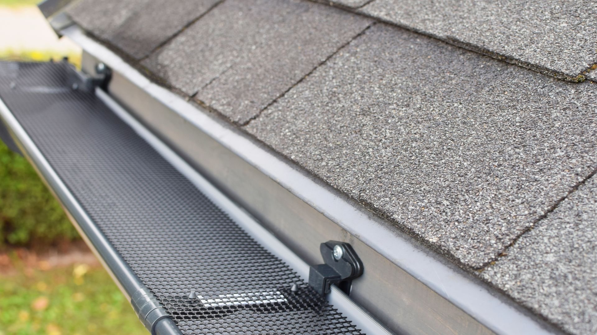 Gutter guard installed on roof edge with textured shingles in background